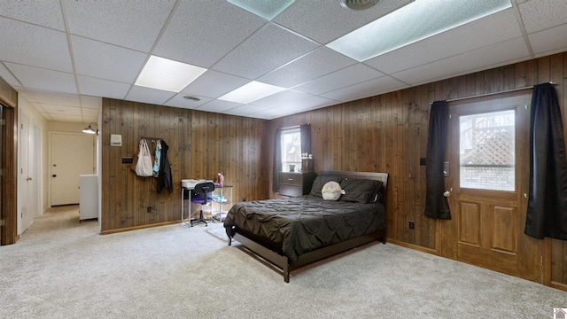 carpeted bedroom with a paneled ceiling and wood walls