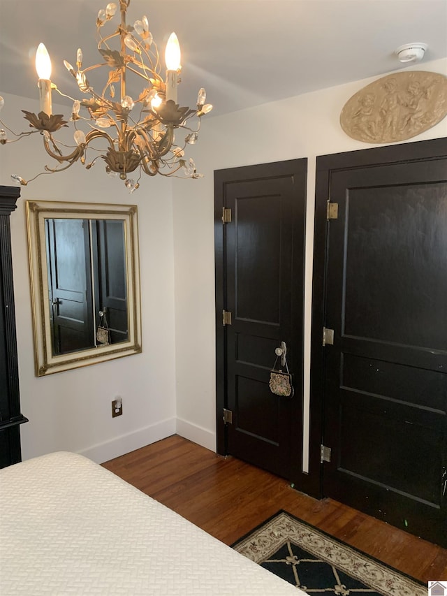 bedroom with dark wood-type flooring, an inviting chandelier, and baseboards