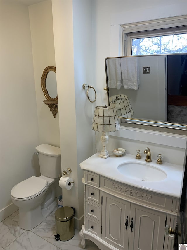 half bathroom with toilet, marble finish floor, baseboards, and vanity