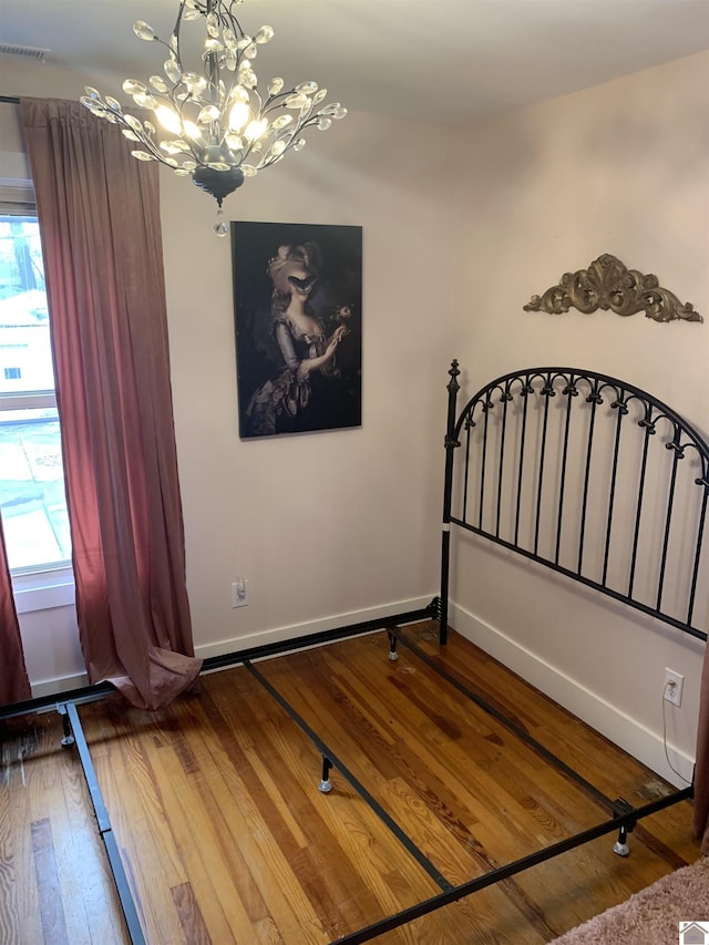 unfurnished bedroom with a chandelier, baseboards, visible vents, and hardwood / wood-style floors