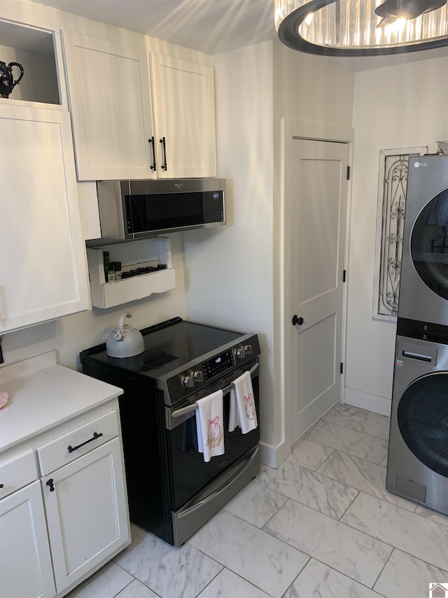 kitchen featuring marble finish floor, stacked washer / dryer, white cabinetry, and electric range oven