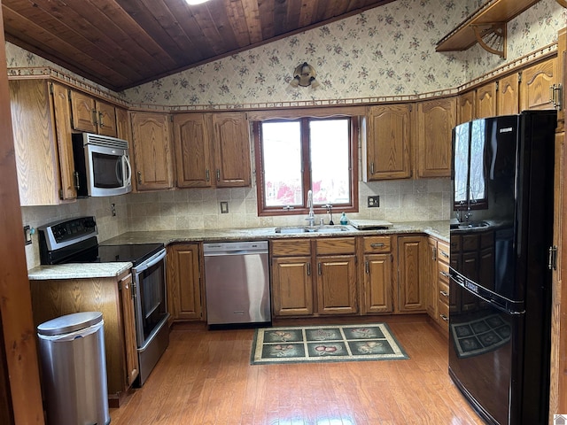 kitchen with lofted ceiling, appliances with stainless steel finishes, a sink, and brown cabinets