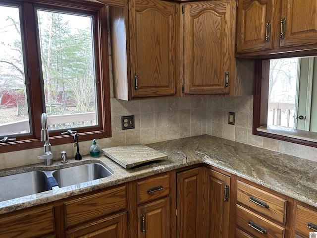 kitchen featuring light stone counters, brown cabinets, and a sink