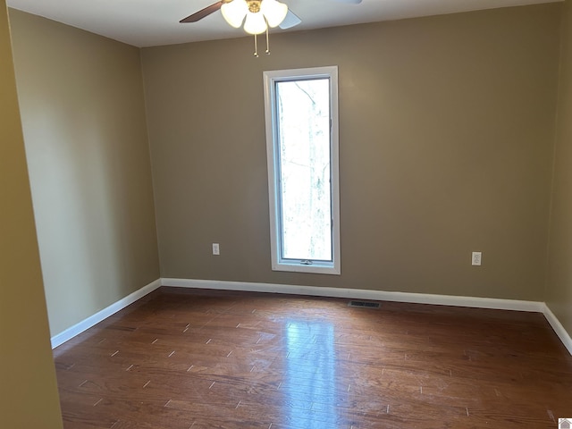 empty room featuring a ceiling fan, visible vents, dark wood finished floors, and baseboards