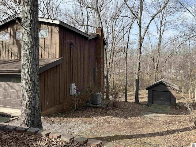 view of side of home featuring cooling unit, a garage, an outdoor structure, dirt driveway, and a chimney