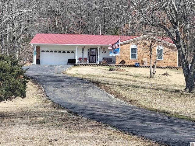 ranch-style house featuring metal roof, aphalt driveway, an attached garage, brick siding, and a front lawn