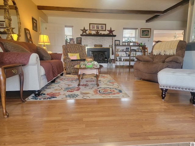 living area featuring a brick fireplace, beamed ceiling, and light wood finished floors