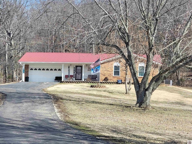 ranch-style home featuring aphalt driveway, brick siding, metal roof, and a garage