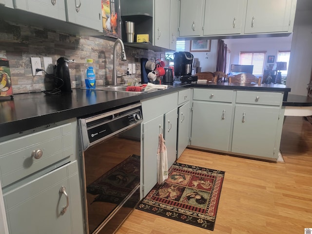 kitchen with a sink, light wood-style floors, backsplash, dishwasher, and dark countertops