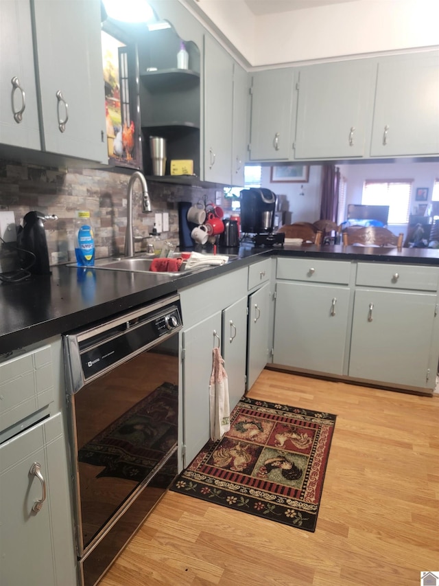 kitchen with light wood finished floors, black dishwasher, tasteful backsplash, dark countertops, and a sink