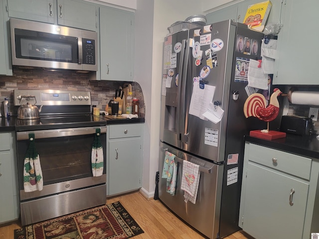 kitchen featuring appliances with stainless steel finishes, dark countertops, backsplash, and light wood finished floors