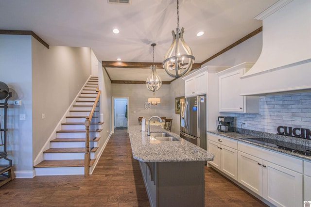 kitchen featuring hanging light fixtures, freestanding refrigerator, a sink, an island with sink, and premium range hood