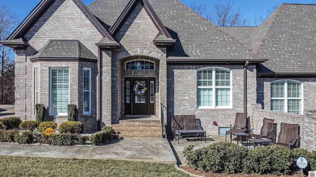 view of front of home featuring brick siding, a patio area, and a shingled roof