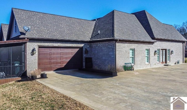 view of side of property with a garage, concrete driveway, brick siding, and roof with shingles