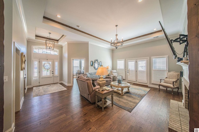 living room featuring dark wood-type flooring, a tray ceiling, crown molding, a fireplace, and a chandelier