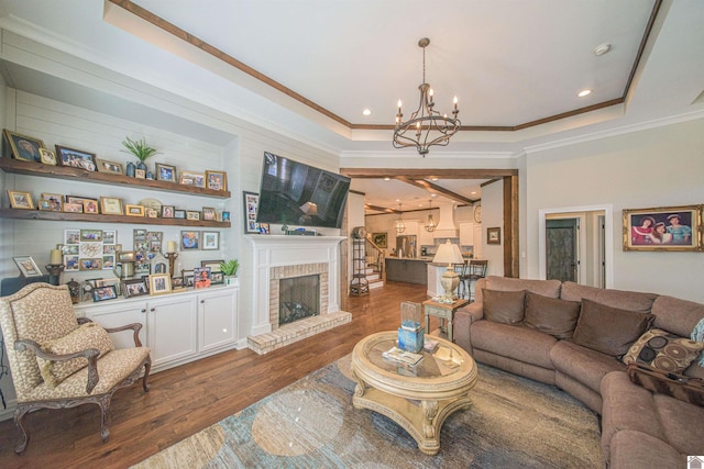 living room with a tray ceiling, dark wood-style flooring, crown molding, an inviting chandelier, and a brick fireplace