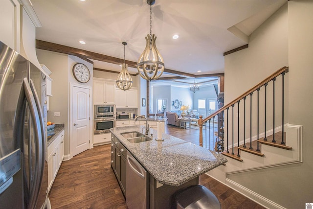 kitchen with stainless steel appliances, a sink, white cabinetry, hanging light fixtures, and a center island with sink