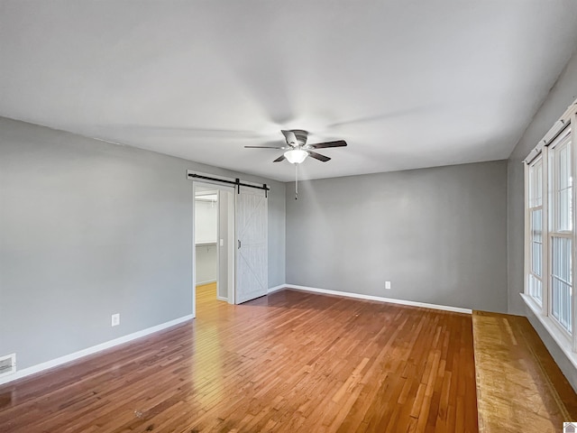 unfurnished room with a barn door, visible vents, baseboards, a ceiling fan, and wood finished floors