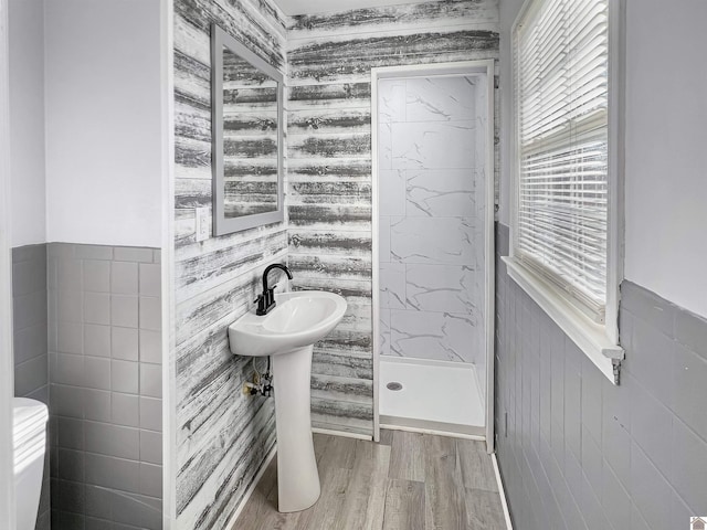 bathroom featuring a wainscoted wall, wood finished floors, walk in shower, and tile walls