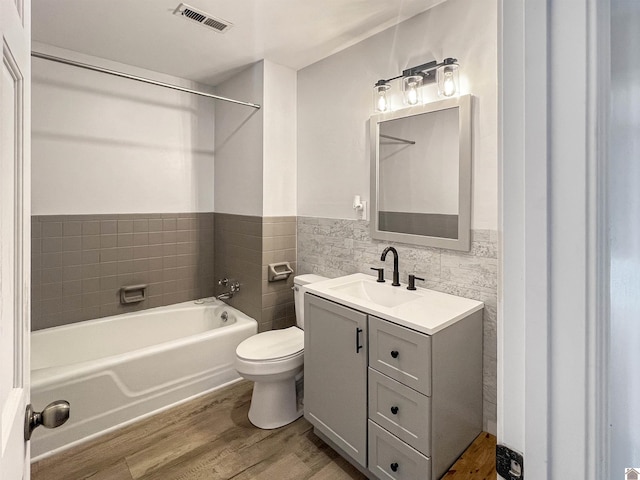 bathroom with tile walls, visible vents, toilet, wainscoting, and wood finished floors