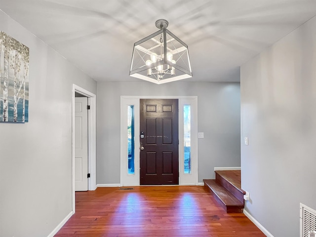 foyer with a notable chandelier, visible vents, stairway, hardwood / wood-style floors, and baseboards