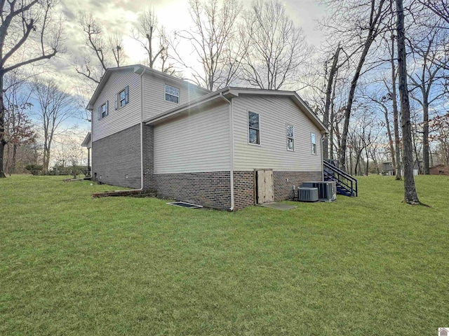 view of side of property featuring cooling unit, brick siding, a lawn, and stairs