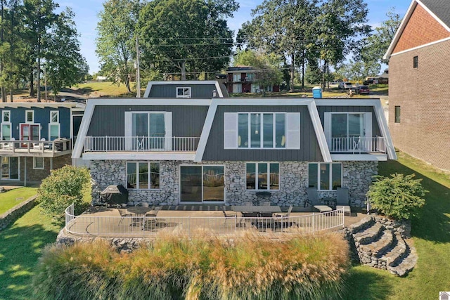 rear view of property with stone siding, a lawn, a patio area, and a balcony