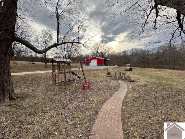 view of yard with driveway, a detached garage, a playground, and an outbuilding