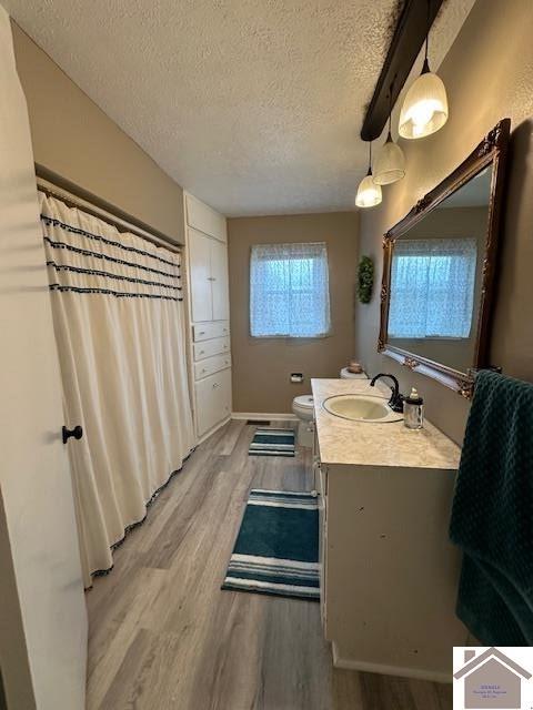 full bath with toilet, a textured ceiling, vanity, and wood finished floors