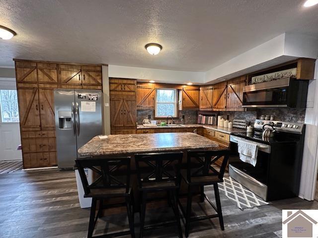 kitchen featuring dark wood-style floors, a barn door, appliances with stainless steel finishes, and brown cabinets