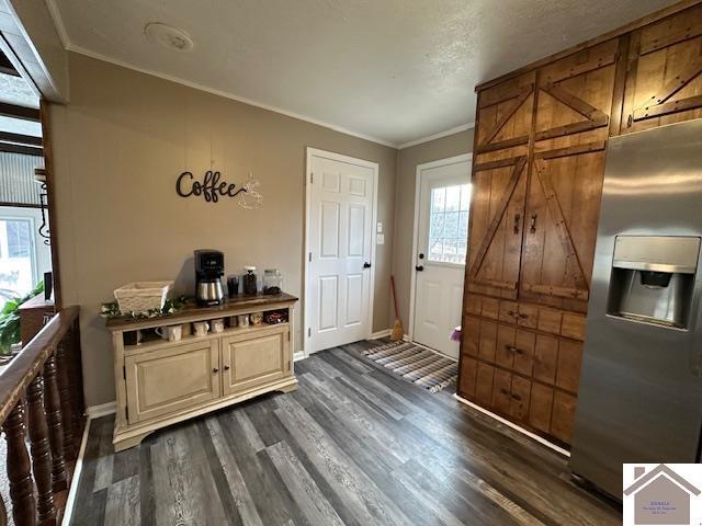 interior space featuring dark wood-style flooring, baseboards, stainless steel fridge with ice dispenser, dark countertops, and crown molding