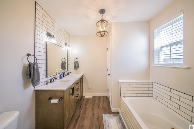 bathroom featuring double vanity, baseboards, toilet, wood finished floors, and a bath