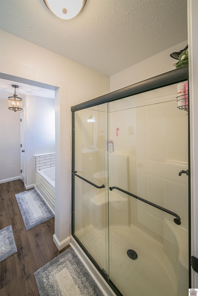 bathroom featuring a textured ceiling, wood finished floors, baseboards, a bath, and a stall shower