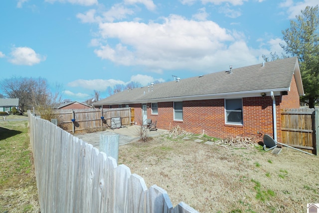 exterior space featuring brick siding, a patio, roof with shingles, a lawn, and a fenced backyard