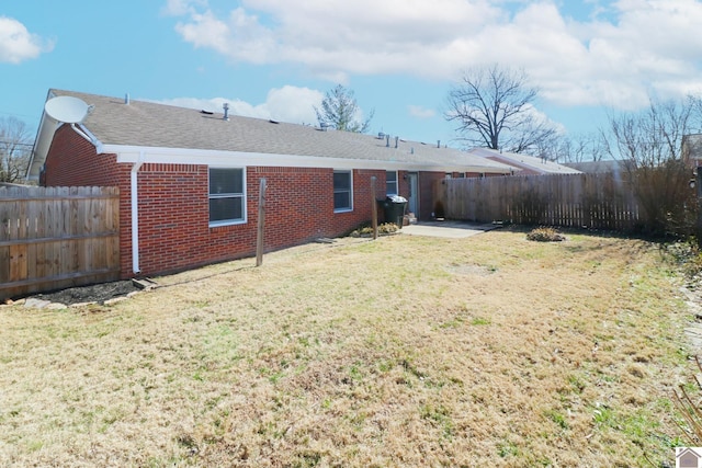 back of property featuring a shingled roof, brick siding, fence, and a lawn