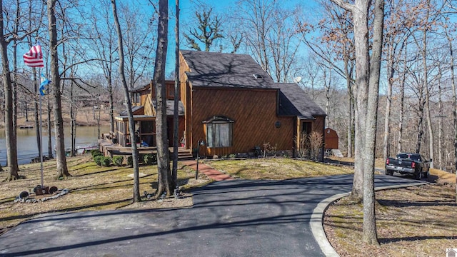 view of side of home with aphalt driveway, a water view, and a shingled roof