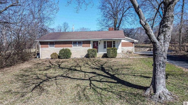 ranch-style house with brick siding, a chimney, covered porch, stone siding, and a front lawn