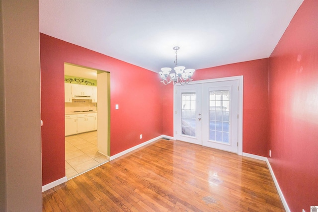 unfurnished dining area with light wood-type flooring, baseboards, a notable chandelier, and french doors