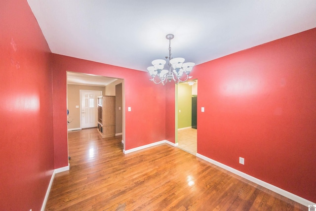 unfurnished dining area with baseboards, a chandelier, and wood finished floors