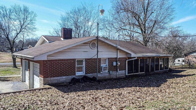 back of property featuring a shingled roof, a chimney, an attached garage, and a sunroom