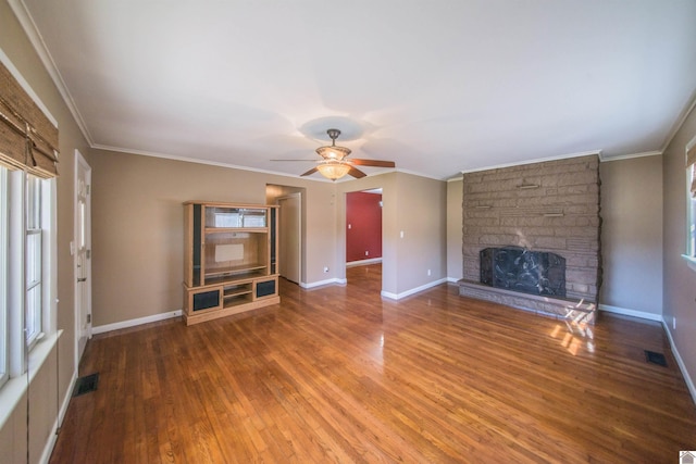 unfurnished living room with baseboards, visible vents, ornamental molding, wood finished floors, and a stone fireplace