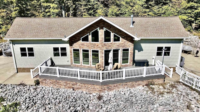 rear view of house with stone siding and roof with shingles