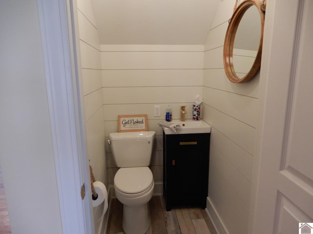 half bath featuring toilet, vaulted ceiling, wood finished floors, and vanity