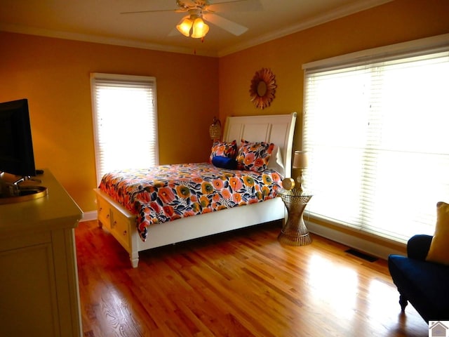 bedroom featuring ornamental molding, multiple windows, wood finished floors, and visible vents