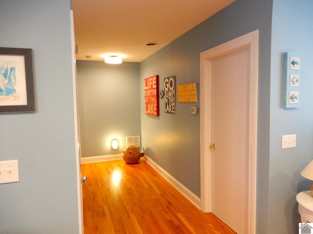 hall with visible vents, baseboards, and wood finished floors