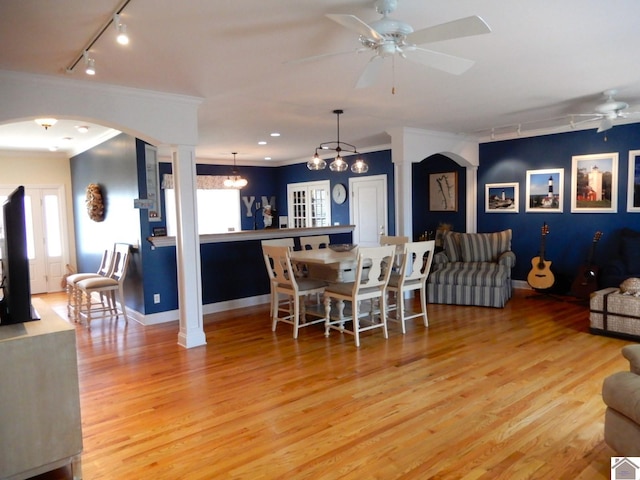 dining space featuring arched walkways, light wood-type flooring, a ceiling fan, and crown molding