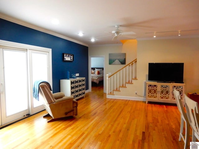 living area featuring crown molding, ceiling fan, wood finished floors, baseboards, and stairs