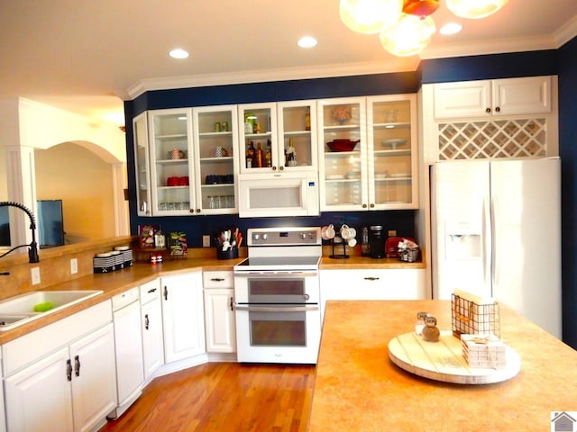 kitchen with white appliances, a sink, white cabinets, light countertops, and crown molding