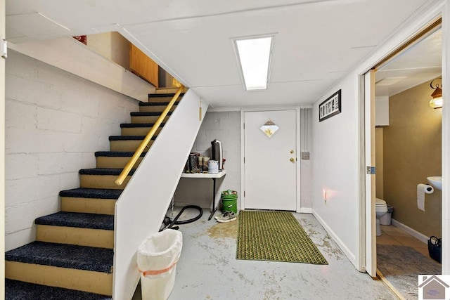 entrance foyer featuring concrete flooring, concrete block wall, baseboards, and stairs