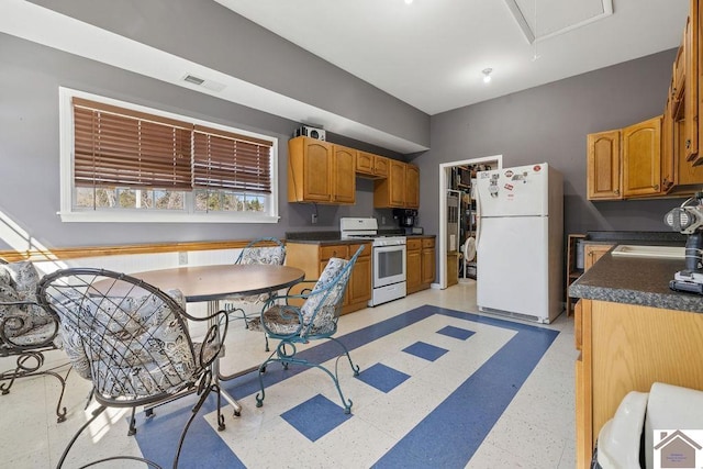 kitchen featuring white appliances, dark countertops, a sink, and visible vents